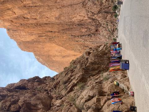      Towering ochre canyon walls flank a narrow road lined with colourful textile stalls.
  