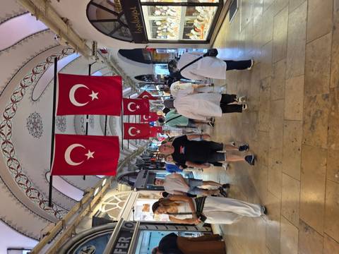       Crowd walking through Grand Bazaar corridor adorned with hanging Turkish flags.
  