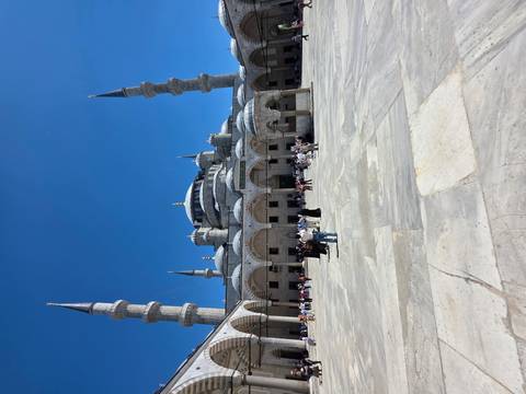       Courtyard view of the Blue Mosque with multiple minarets under clear blue sky.
  