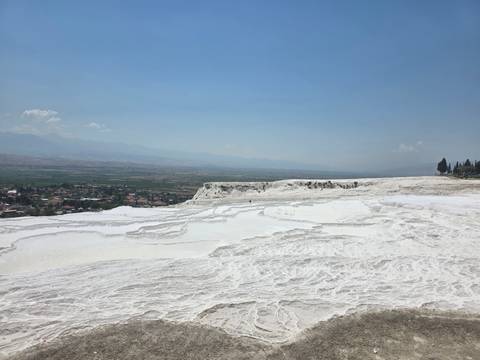       White travertine terraces of Pamukkale overlooking vast plain under blue sky.
  