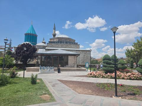      Exterior of Mevlana Museum complex in Konya with gardens, flowers and turquoise dome.
  