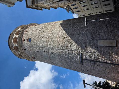       Tall stone Galata Tower rising against bright blue sky in Istanbul.
  