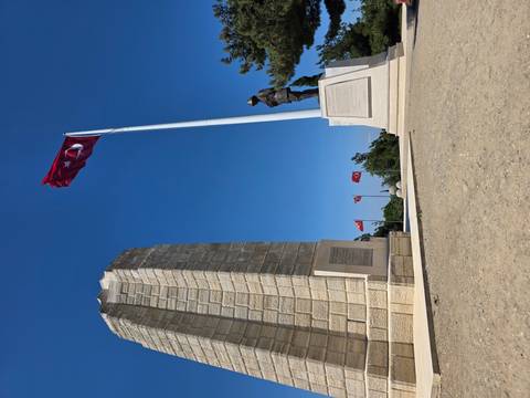       Gallipoli memorial with Turkish flags and soldier statue under clear sky.
  