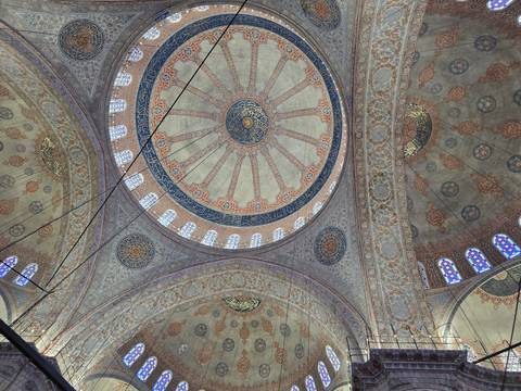       Intricate domes and floral patterns of the Blue Mosque ceiling viewed upward.
  