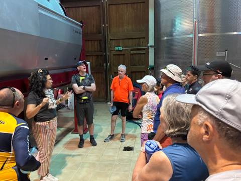       Guide explaining wine-making equipment inside a winery to a tour group.
  
