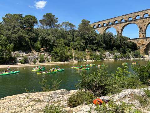       Dozens of kayakers paddling on a river beneath the ancient Pont du Gard aqueduct.
  