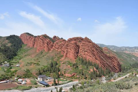       Jagged red sandstone ridges of Jeti-Ögüz Valley framed by green forest and village below
  