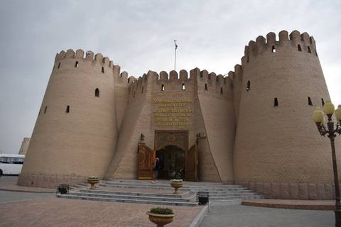       Historic Ark Fortress entrance in Bukhara with tall mud-brick walls under blue sky
  