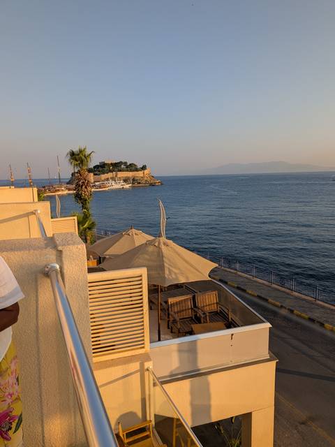       Seaside view at sunset with an island fortress and calm blue waters seen from a terrace with umbrellas
  