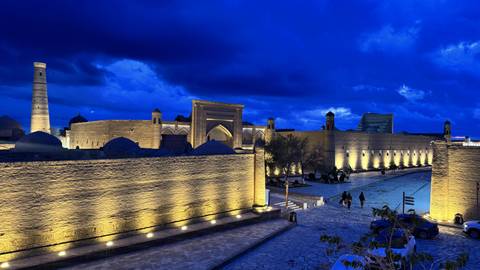       Evening view of ancient mud-brick city walls and minarets illuminated under deep blue sky
  