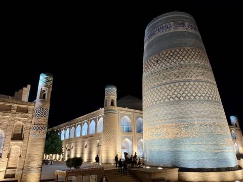       Historic madrasah and tall patterned minaret lit warmly against dark sky
  