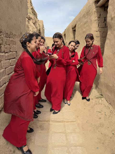       Group of young women in matching red traditional dresses laughing in narrow adobe alley
  