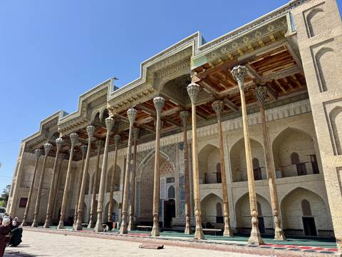       Wood-columned mosque façade with intricate ceiling carvings under clear sky
  