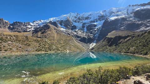       Crystal-clear turquoise Humantay Lake mirroring snow-capped Andean peaks under a deep blue sky.
  