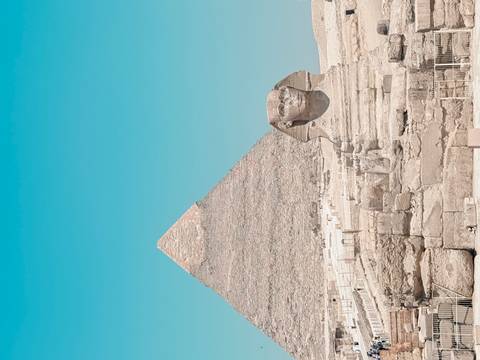       Iconic view of the Great Sphinx with a pyramid rising behind under a clear blue sky.
  