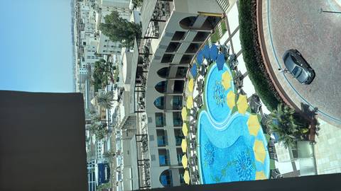      Bird’s-eye view from a hotel window of a large lagoon-style pool surrounded by yellow umbrellas in a city setting.
  