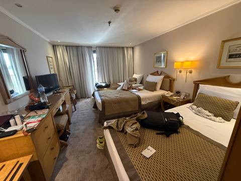      Interior of a somewhat cluttered twin hotel room with luggage and belongings scattered on the beds.
  
