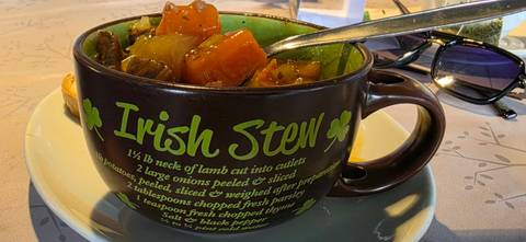       Hearty bowl of Irish stew with vegetables in a mug labeled 'Irish Stew' on a restaurant table.
  