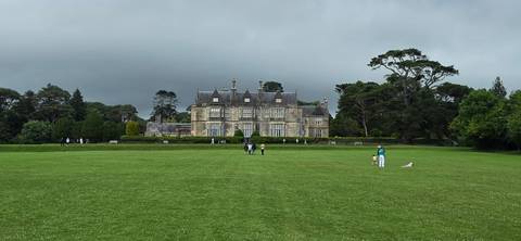       Expansive green lawn leading to stately Muckross House framed by dark clouds in Killarney National Park.
  
