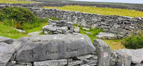       Ancient stone walls and inscribed rock amid rolling green fields on the Aran Islands
  