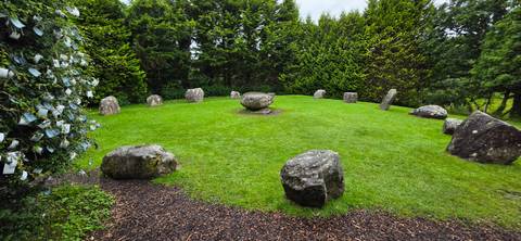       Small stone circle with upright boulders on manicured grassy clearing among tall trees
  