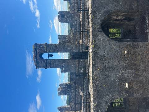       Stone bell tower framed by castle ruins against a bright blue sky in Ireland
  
