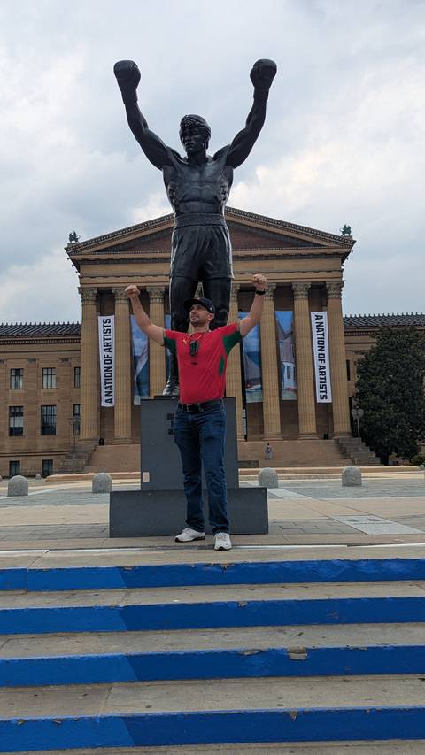       Man posing victoriously in front of a large statue with classical museum columns behind
  