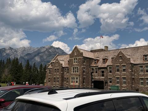       Historic stone building in Banff set against rugged mountain backdrop and partly cloudy sky.
  