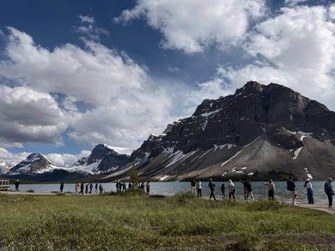       Visitors stand along the shore of Bow Lake with dramatic rocky peaks rising sharply behind.
  