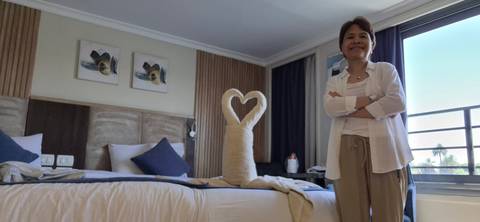       Guest standing beside a neatly made hotel bed decorated with towel art shaped like a heart.
  