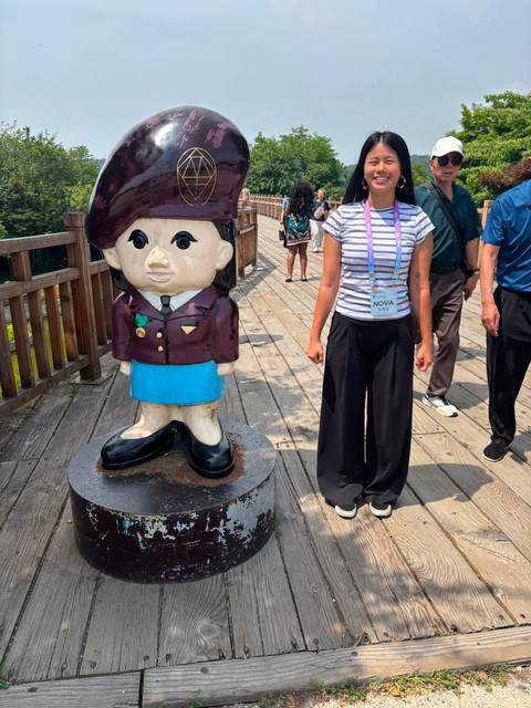       Woman stands next to a cute cartoon soldier statue on an outdoor wooden walkway
  