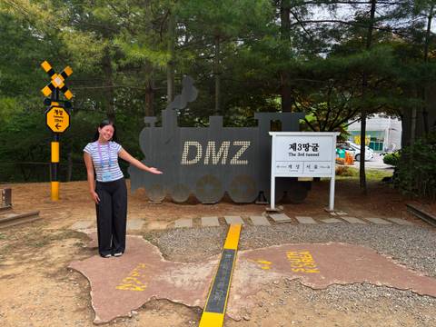       Woman gestures toward a DMZ locomotive cut-out sign at an outdoor exhibit
  