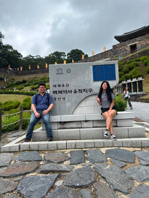       Repeat shot of travellers seated by the UNESCO Baekje Historic Areas stone sign
  