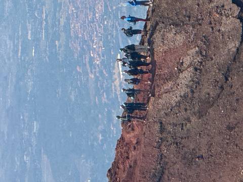       Small hiking group standing on the rim of a reddish volcanic crater high above the valley below.
  