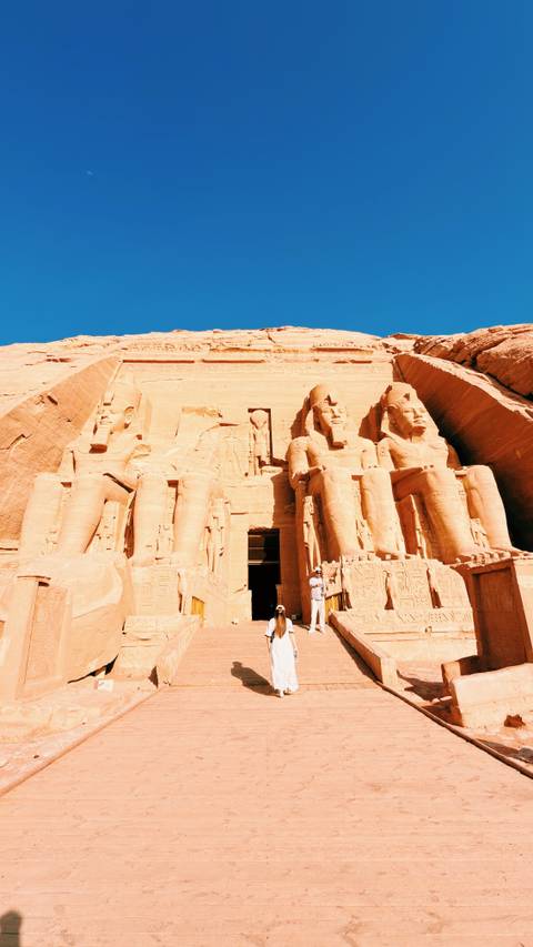       Grand façade of Abu Simbel with colossal statues carved into sandstone cliff under clear sky
  