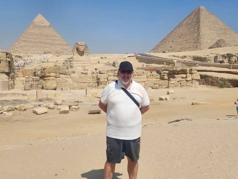       Tourist posing in front of the pyramids and Sphinx on a bright desert day
  