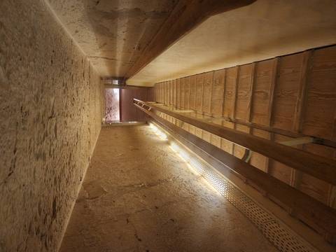       Wooden stairway descending deep inside a pyramid passage with low lighting
  