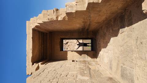       Silhouetted person raising arms in a doorway of Philae ruins against clear sky
  