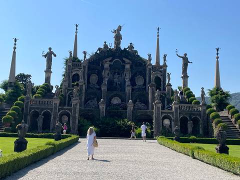       Baroque terraced garden with statues and obelisks on Isola Bella as visitors stroll below.
  