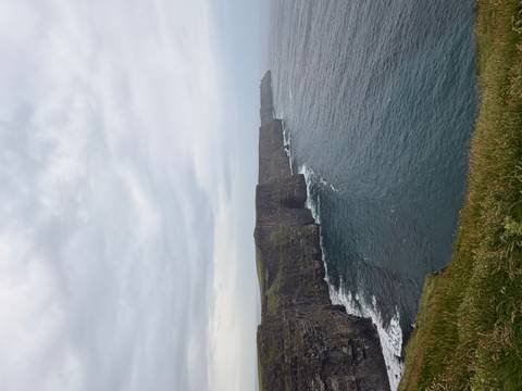      Iconic vertical cliffs plunging into Atlantic Ocean at the Cliffs of Moher under gray sky
  