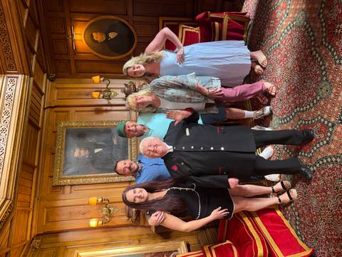       Group portrait inside ornate wood-paneled room with historic portraits and patterned carpet
  