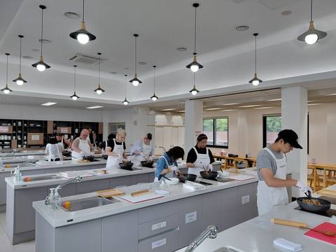      Cooking class with participants preparing dishes at individual workstations in a bright modern kitchen
  
