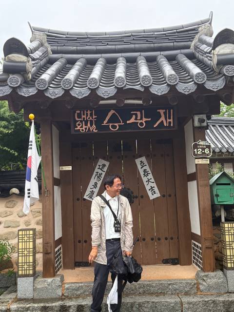      Smiling guide standing by a traditional Korean wooden gate with hangul calligraphy panels
  