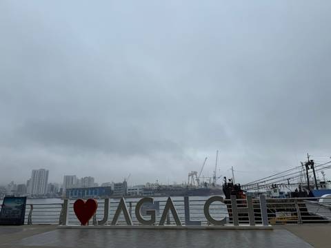       Cloudy waterfront scene showing city buildings, cranes at an industrial port and an “I ❤️” sign in the foreground.
  