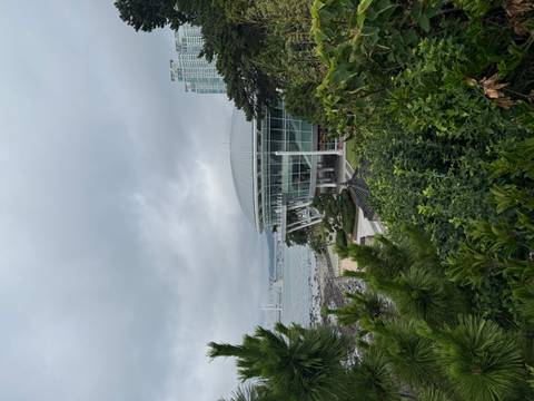       Modern glass-walled rotunda on a coastal cliff with sea, bridge and city skyline partially visible under grey clouds.
  