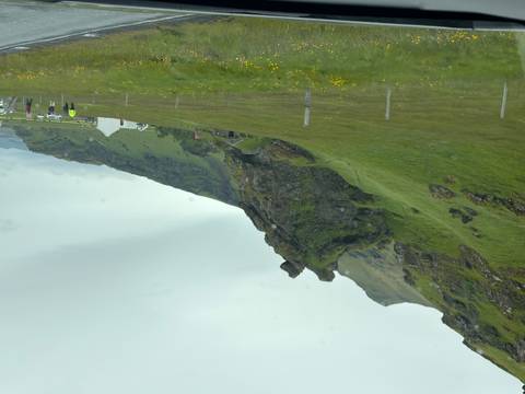       Lush green hillside with an unusual rock formation resembling an animal head near rural Icelandic farms
  