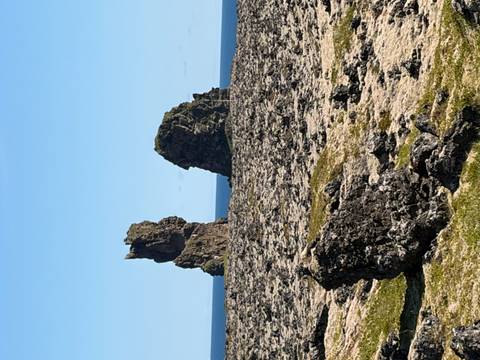       Two tall volcanic sea stacks rising from a barren lava field against a clear blue sky and distant sea
  