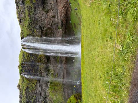       Full frontal view of Seljalandsfoss waterfall cascading over a mossy cliff into a green meadow
  
