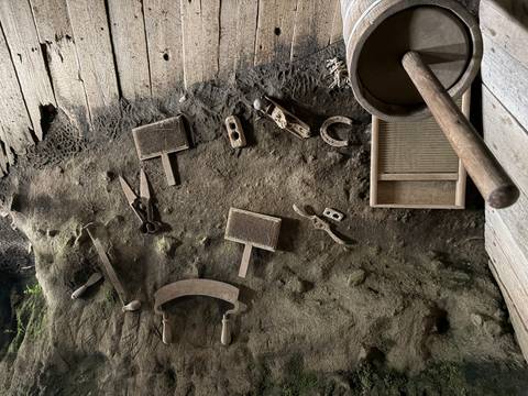       Old handmade tools and objects embedded in an earthen cave wall with dusty wooden floor
  