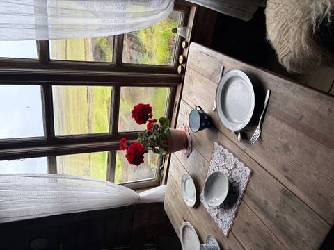       Rustic wooden table set for two beside a cottage window overlooking Icelandic marshland
  